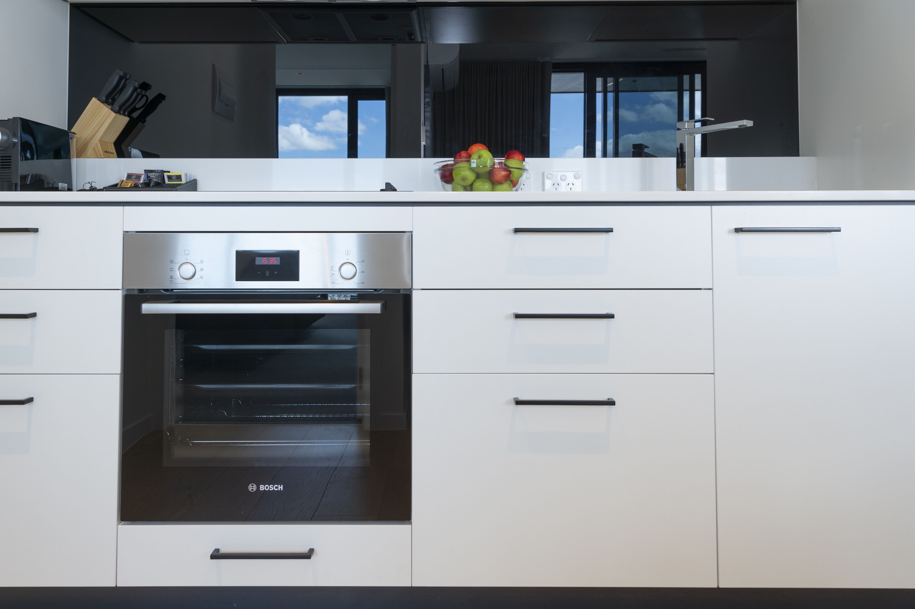 Een moderne keuken met een Bosch oven, witte kastjes en een fruitschaal op het aanrecht.