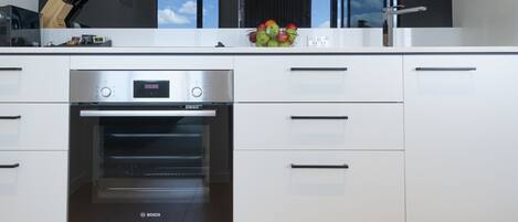 A modern kitchen with a Bosch oven, white cabinets, and a fruit bowl on the countertop.