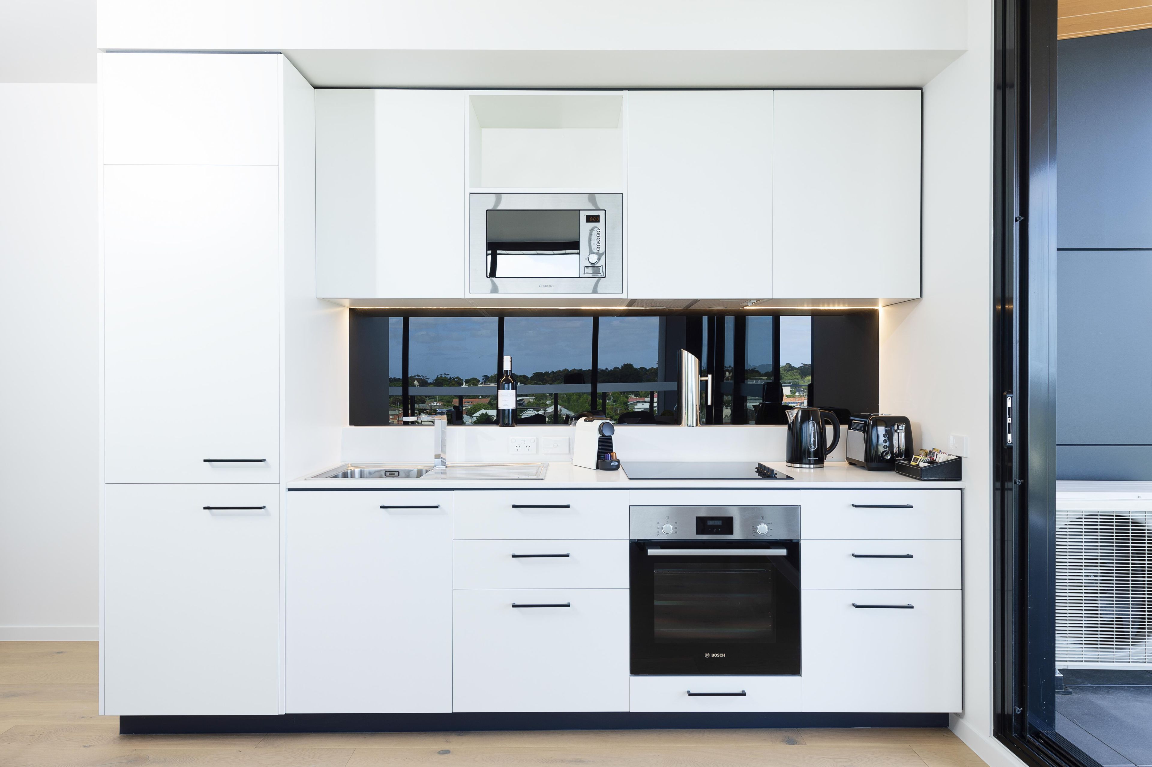 Una cocina moderna con armarios blancos, un horno Bosch y un microondas.