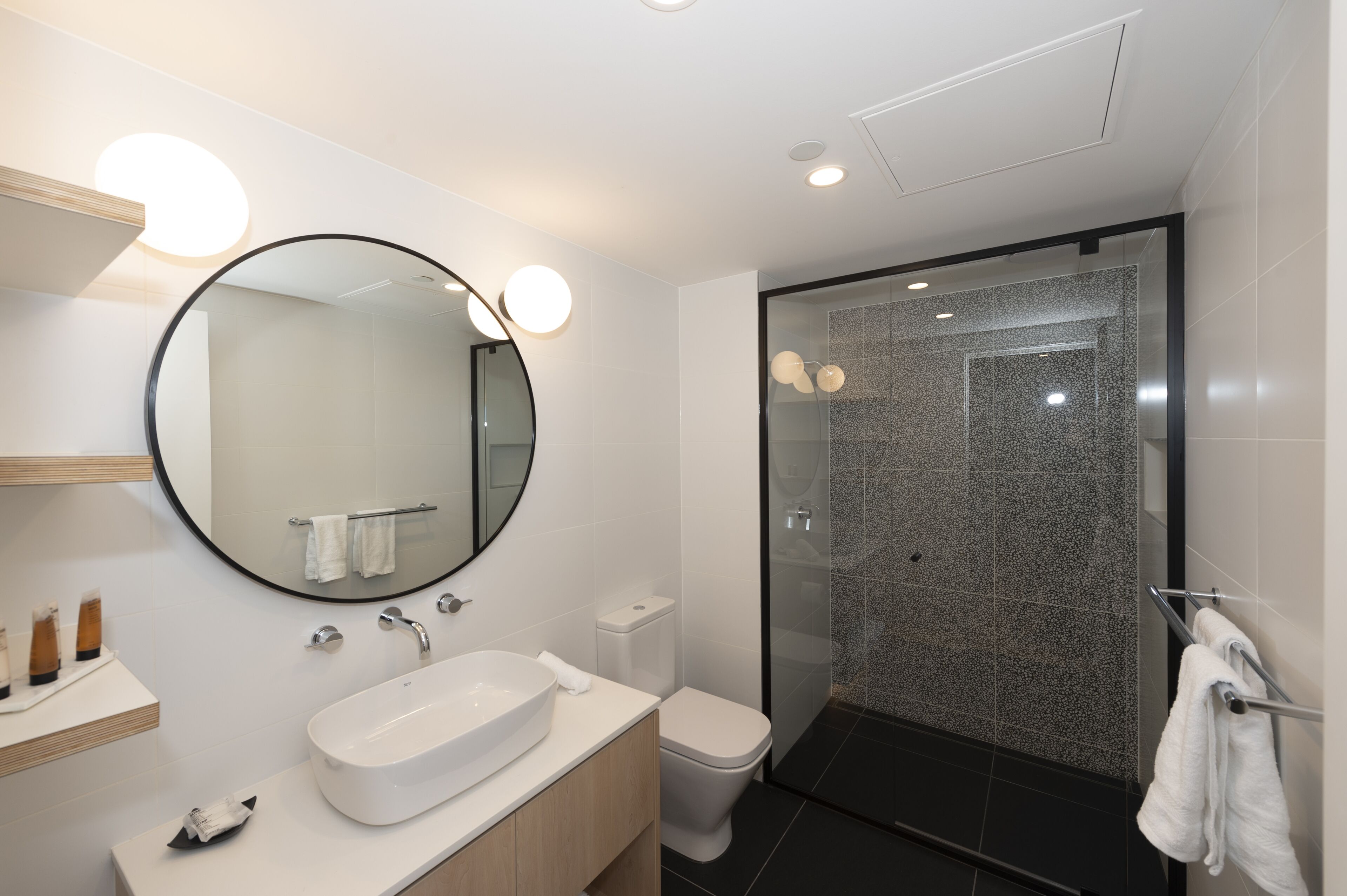 Un baño moderno con un espejo redondo, lavamanos blanco y cabina de ducha de vidrio.