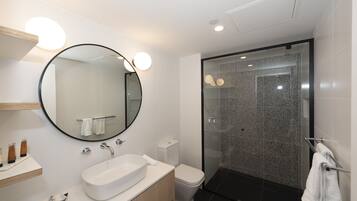 Un baño moderno con un espejo redondo, lavamanos blanco y cabina de ducha de vidrio.