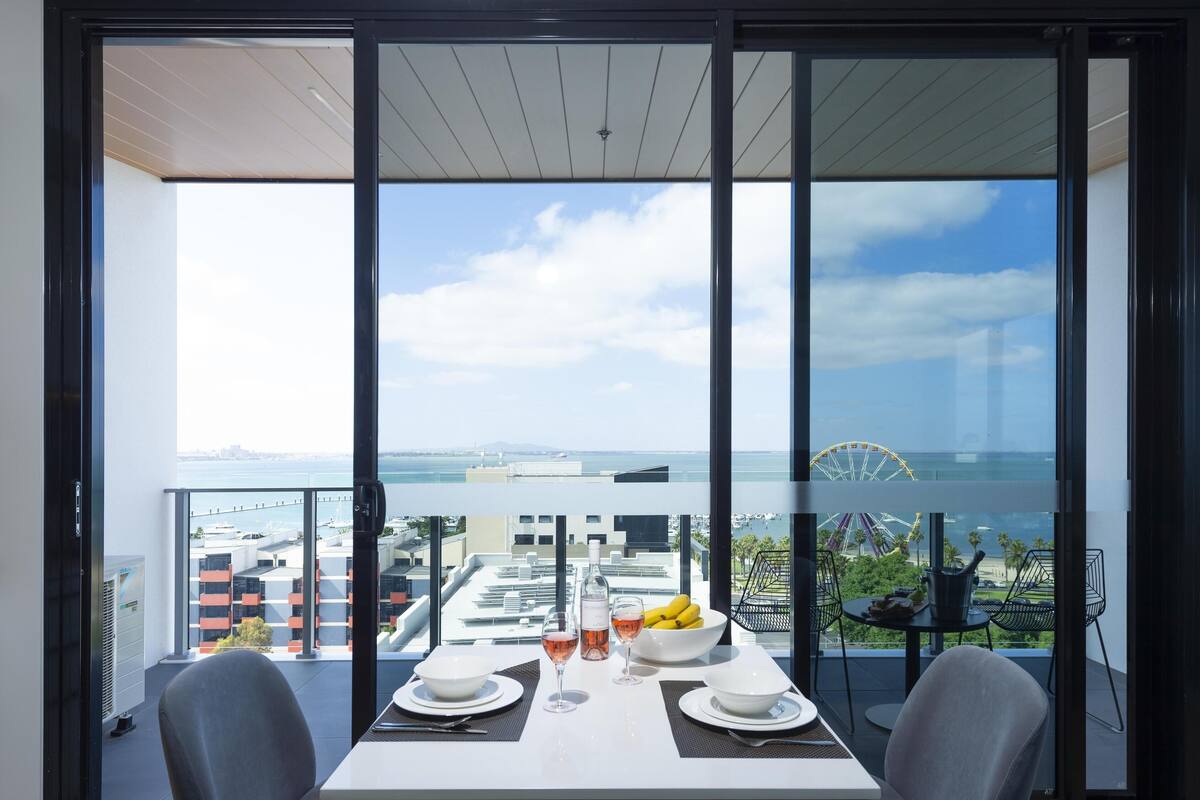 A dining area with a table set for two, a bottle of wine, and a bowl of fruit.