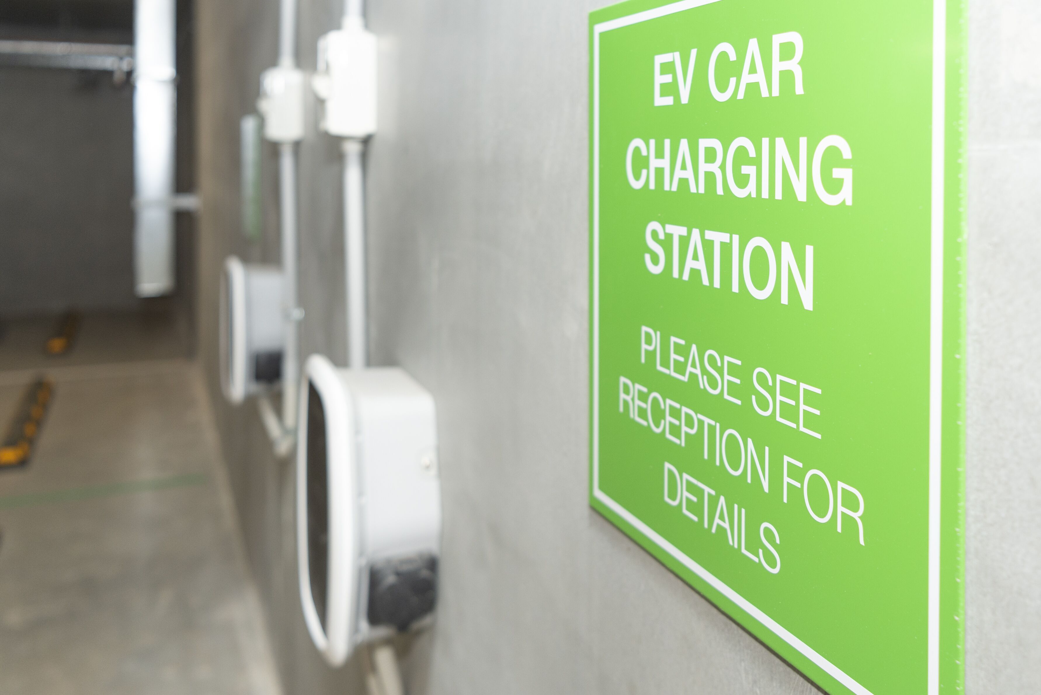 Grünes Schild, das eine Ladesäule für Elektroautos kennzeichnet. Bitte informieren Sie sich am Empfang über Details.