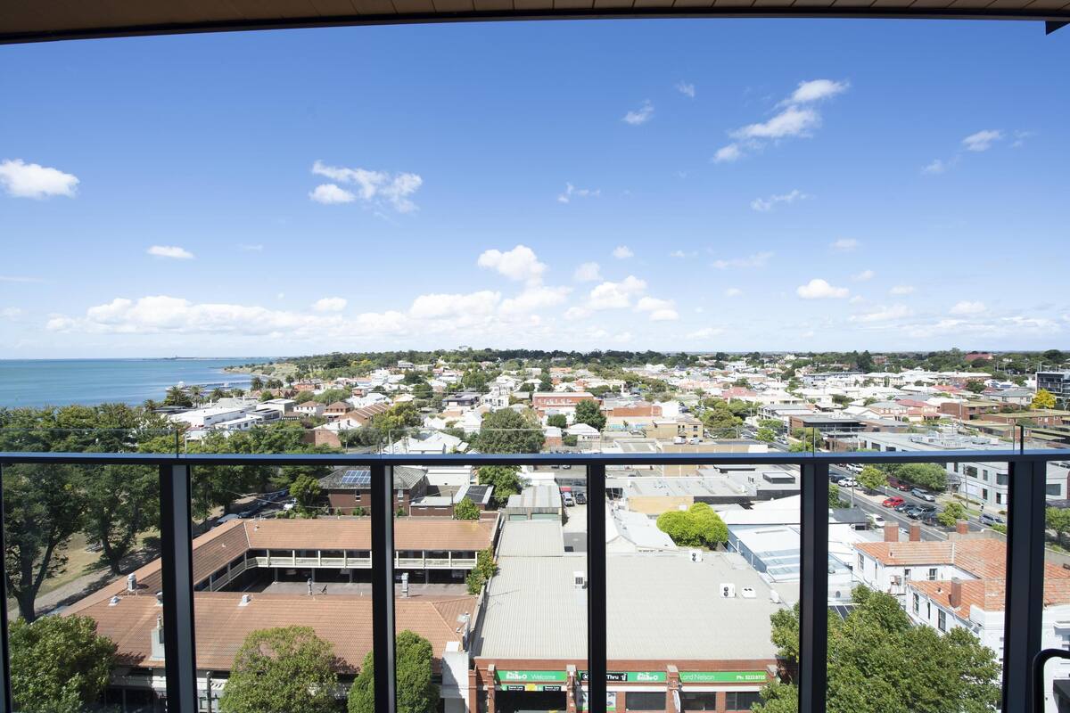 A coastal town with a mix of residential and commercial buildings, a clear sky, and a view of the sea.