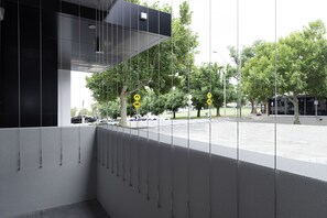 A modern building with a glass facade, a parking lot, and trees in the background. - Oaks R Suites Geelong (Geelong)