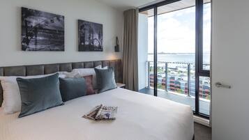 Une chambre d’hôtel avec un grand lit, deux œuvres d’art accrochées au mur, une fenêtre donnant sur la ville et un balcon avec une balustrade.