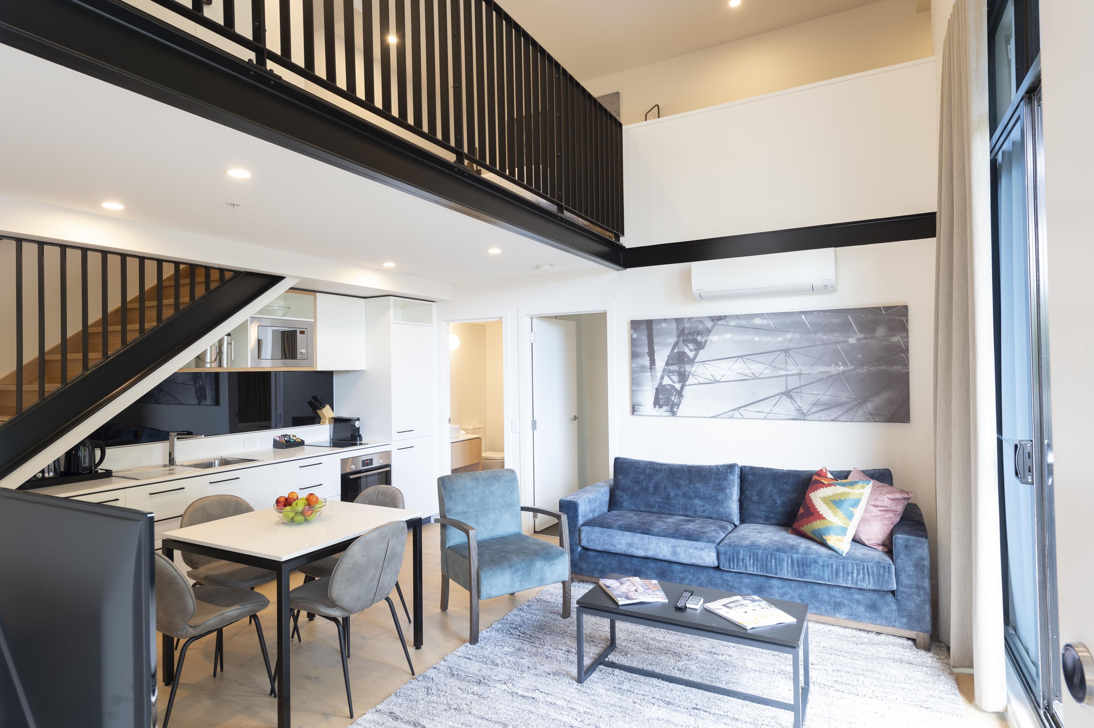 A modern interior with a dining area, kitchen, and living space, featuring a staircase and a large window.