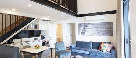 A modern interior with a dining area, kitchen, and living space, featuring a staircase and a large window.