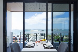 A balcony with a table set for two, a bottle of wine, and a bowl of fruit.