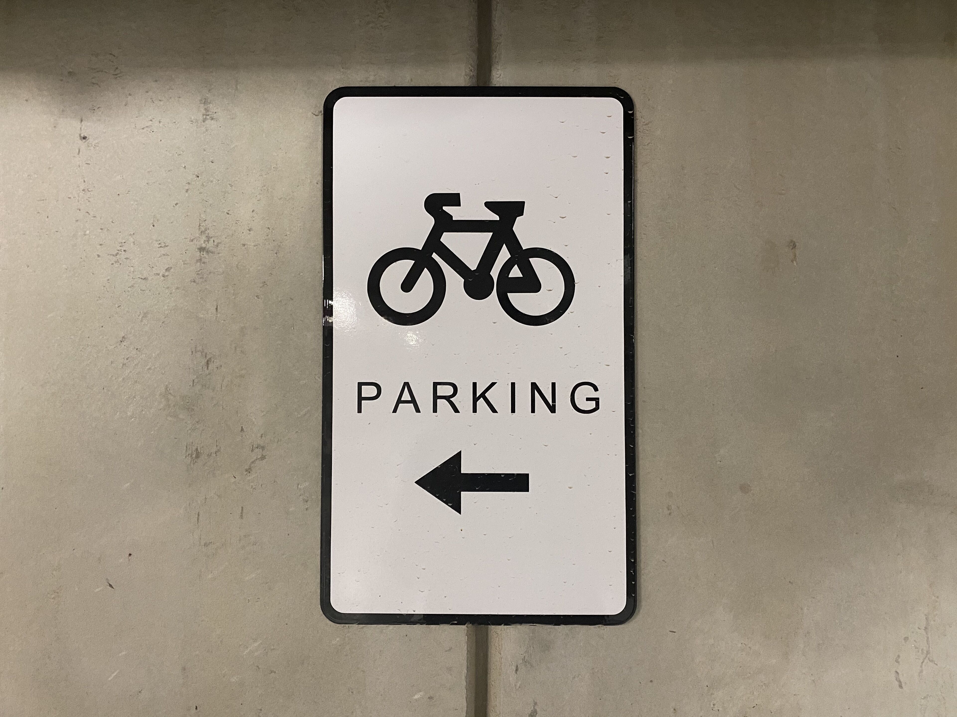A parking sign with a bicycle symbol and an arrow pointing to the left.