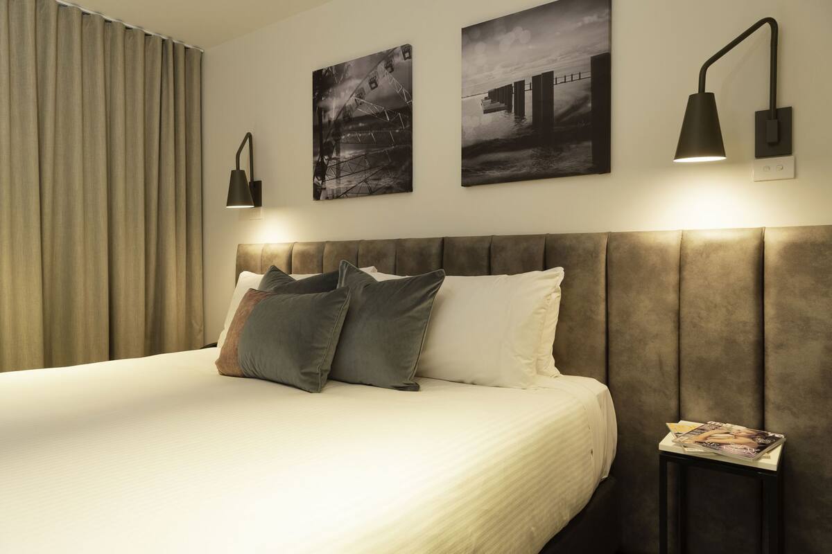 A hotel room with a bed, two wall-mounted lamps, and two framed pictures.
