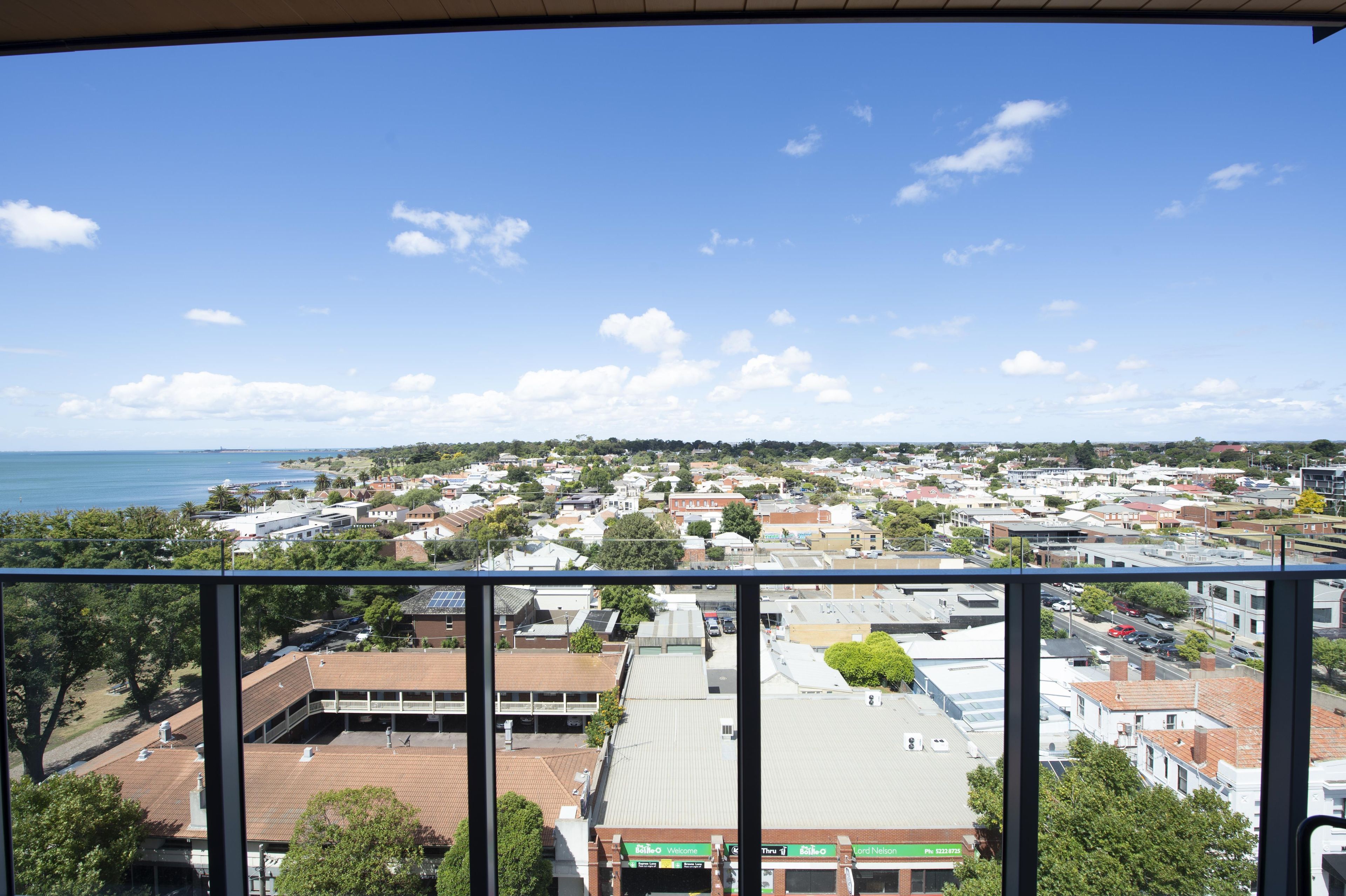 A coastal town with a mix of residential and commercial buildings, a clear sky, and a view of the sea.