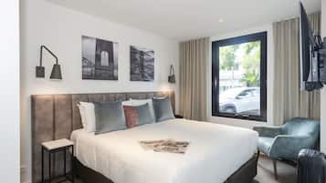 A hotel room with a large bed, a small table, a chair, a TV, and a window with a view of the street.