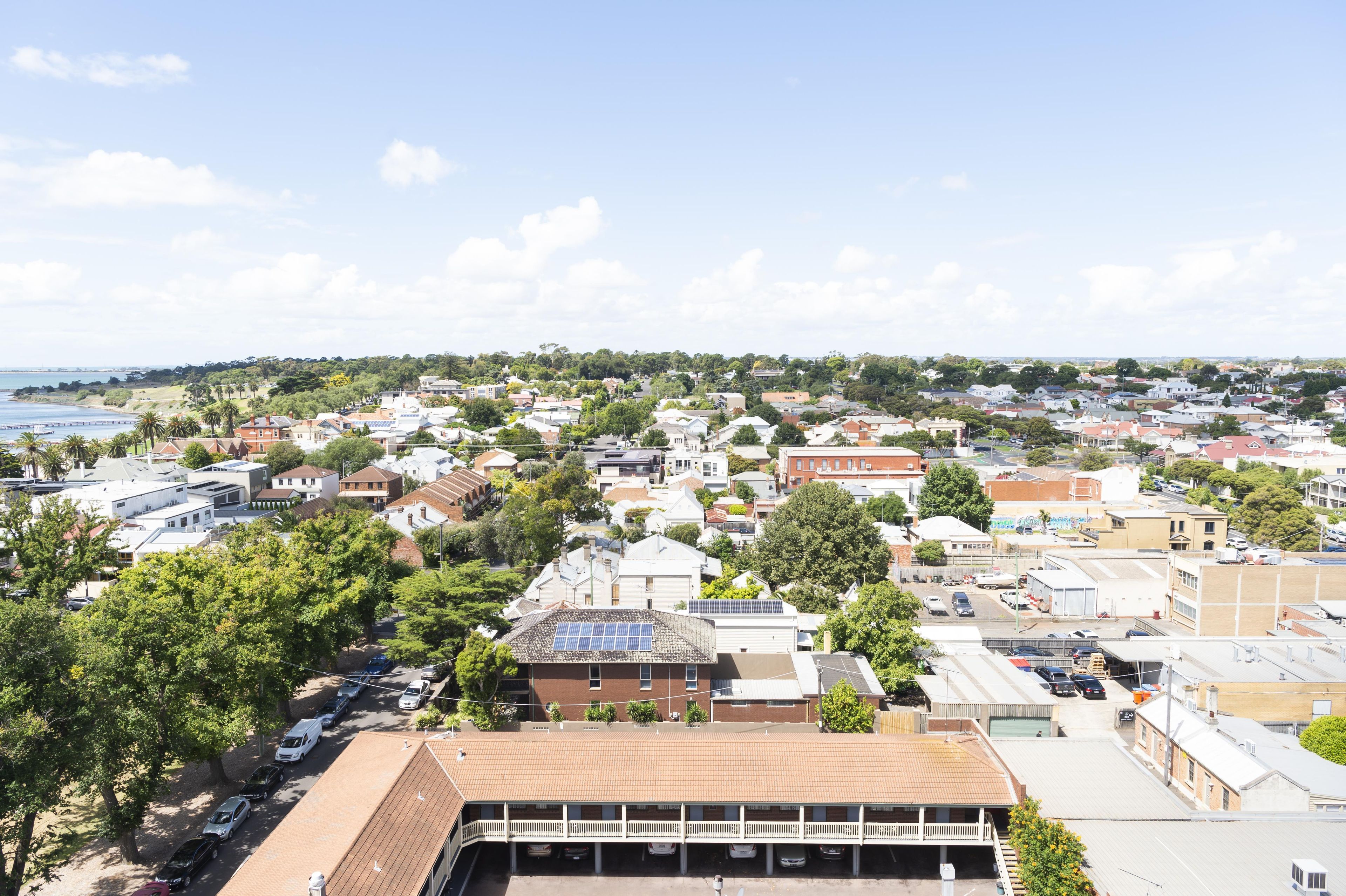 A residential area with a mix of houses and commercial buildings, a clear sky, and a body of water in the distance.