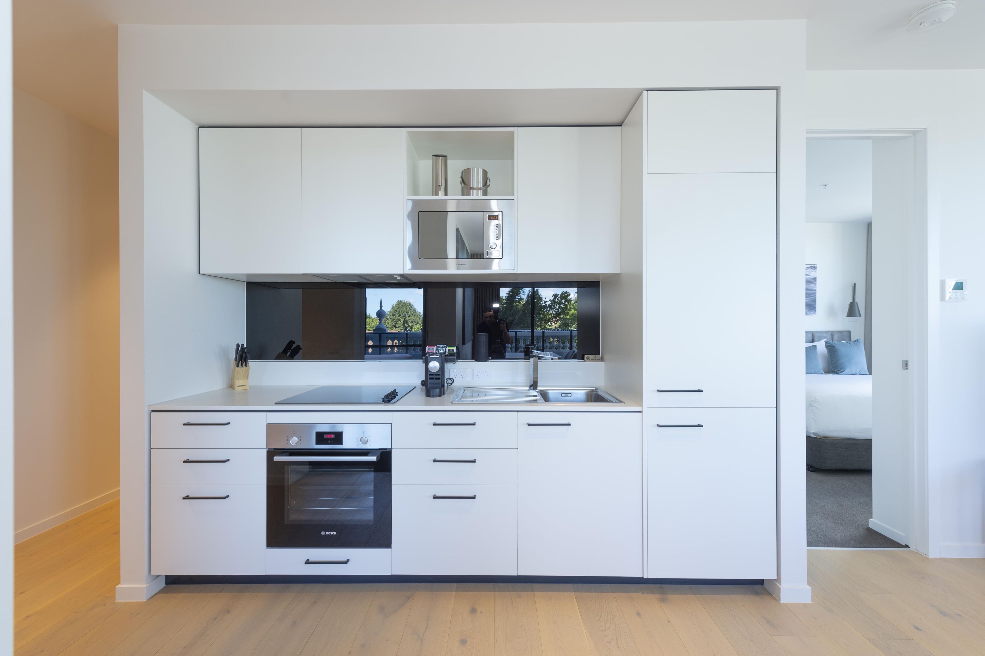 Een moderne keuken met witte kasten, een Bosch oven, een inbouwmagnetron en een roestvrijstalen afzuigkap.