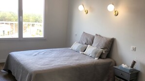 Une chambre à coucher comprenant un lit, deux lampes fixées au mur, une table de chevet et une fenêtre avec des stores.