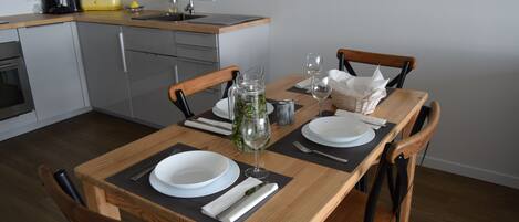 Un comedor con una mesa de madera dispuesta para dos personas, incluyendo platos, cubiertos y una jarra de agua.