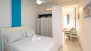 A hotel room with a bed, a bathroom with a shower, and a dining area with chairs.