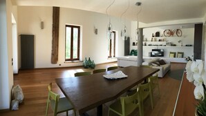 A spacious living area with a wooden dining table, green chairs, a sofa, and a television.