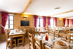 A dining area with wooden tables and chairs, a chalkboard sign, and red curtains. - Terresens - Hotel Escapade (Huez)