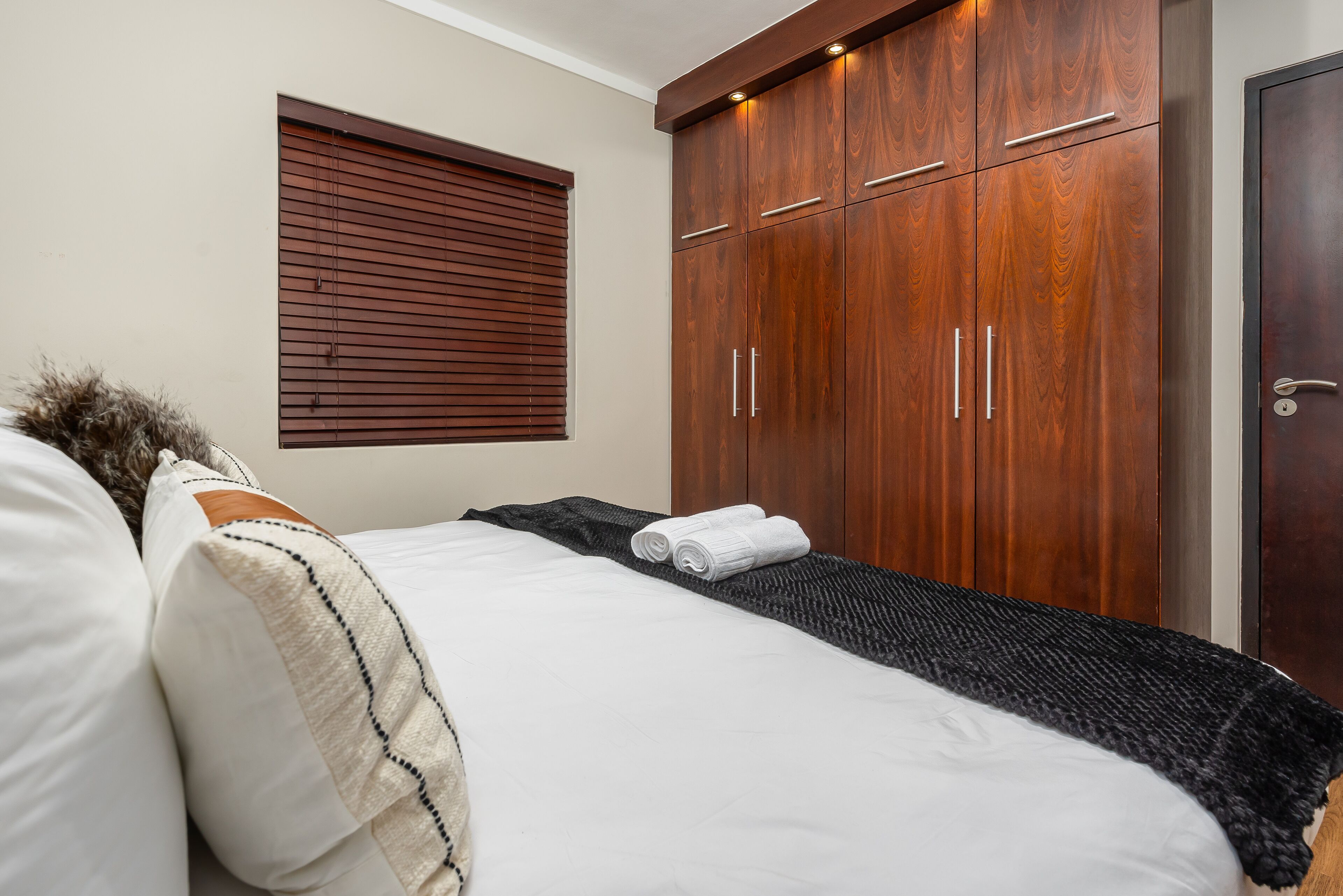 A bedroom with a bed, a window with blinds, a wardrobe, and a door.