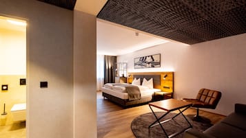 A modern hotel room with a large bed, a desk, and a comfortable armchair.
