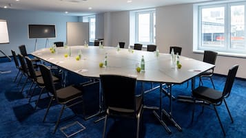 Un salón de conferencias con una mesa grande, sillas, un proyector y una pantalla.