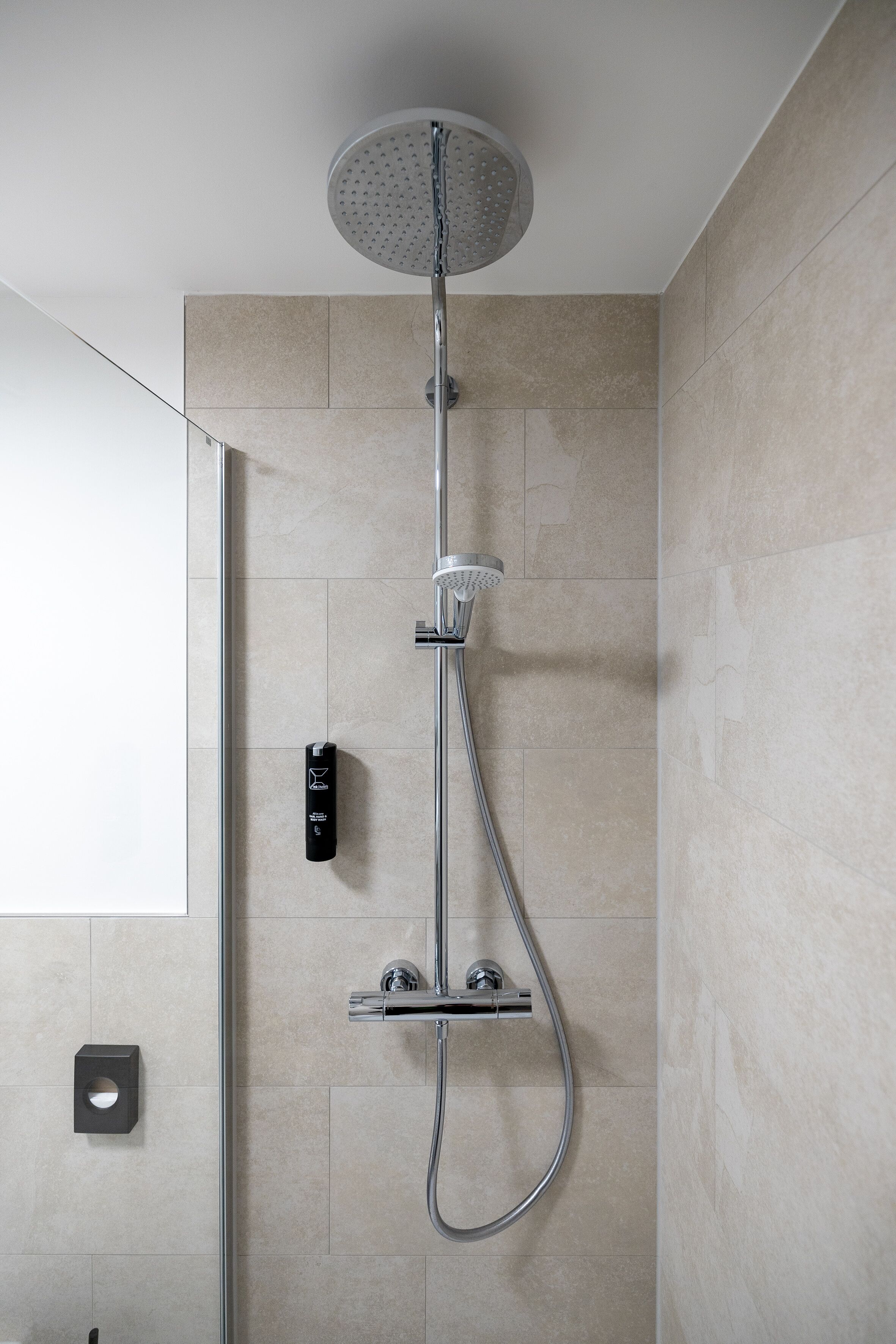 A modern shower with a handheld showerhead and a wall-mounted control panel.