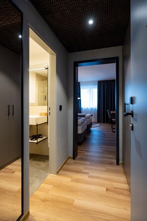 A modern hotel room with a wooden floor, a bed, a desk, and a bathroom visible through an open door. - mk | hotel passau (Passau)