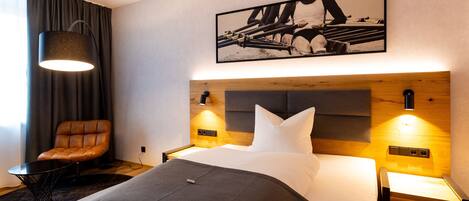 Una habitación de hotel moderna con una cama bien hecha, un sillón de cuero, una mesita y un cuadro colgado en la pared.