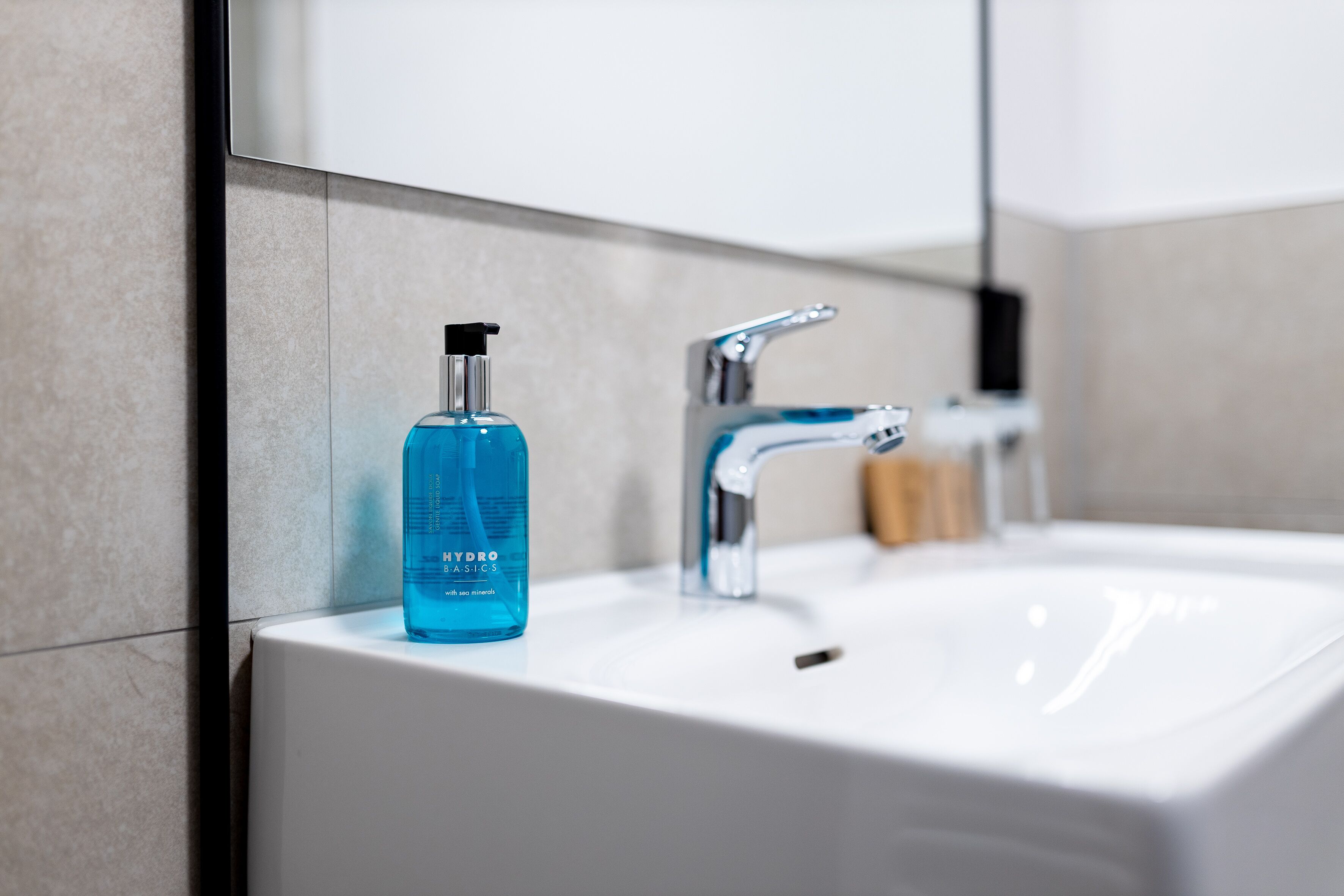 Un baño con un lavamanos blanco, un dispensador de jabón azul y un grifo de cromo.