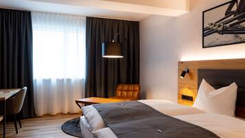 A hotel room with a bed, a desk, a chair, a lamp, and a painting on the wall.