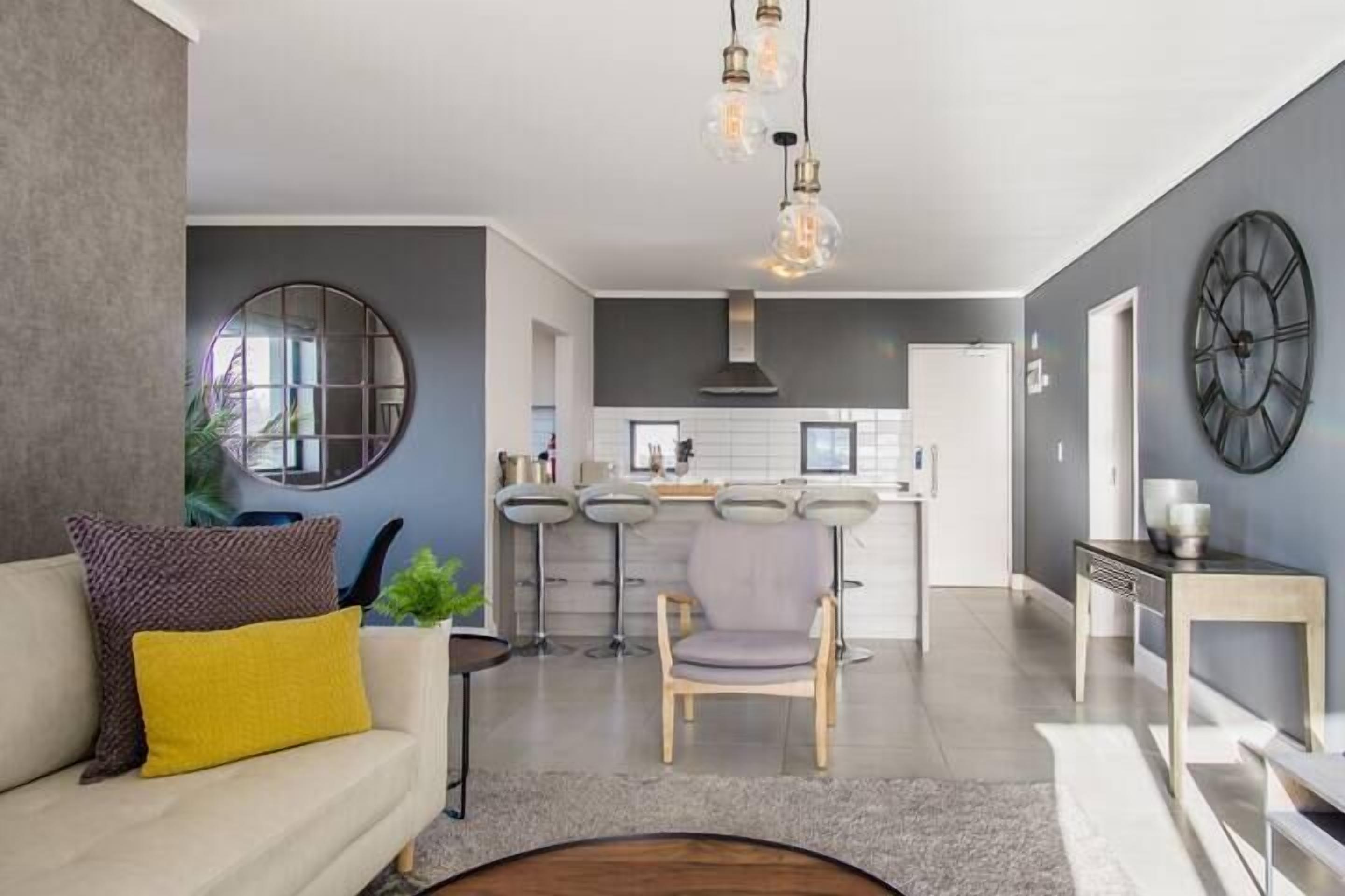 A modern living room with a sofa, a coffee table, and a dining area with bar stools.