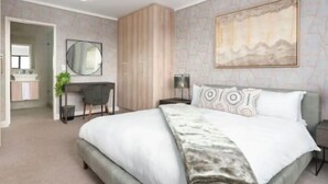 A modern bedroom with a large bed, a desk, a wardrobe, and a painting on the wall. - Waters Edge 503 (Cape Town)