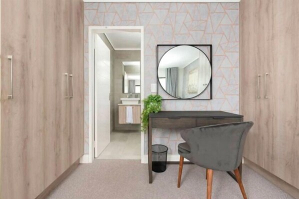 A modern room with a wooden wardrobe, a round mirror on the wall, a grey chair, and a small table with a plant.