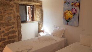 A bedroom with a stone wall, a window with shutters, a bedside table with a lamp, and a painting of balloons. - Casa Dr. Saba (Belmonte, Portugal)