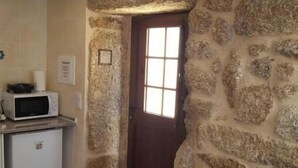 A compact kitchen with a stone wall, a small refrigerator, and a microwave on the counter. - Casa Dr. Saba (Belmonte, Portugal)