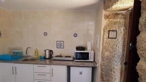 A compact kitchen with white cabinets, a sink, a kettle, a microwave, and a small refrigerator. - Casa Dr. Saba (Belmonte, Portugal)