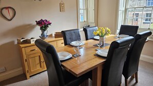 Une salle à manger avec une table en bois dressée pour quatre personnes, des chaises noires, un vase rempli de fleurs et un miroir au mur.