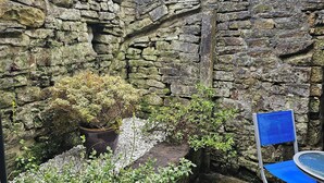 Une cour bordée de murs en pierre, avec une chaise bleue et des plantes en pot.