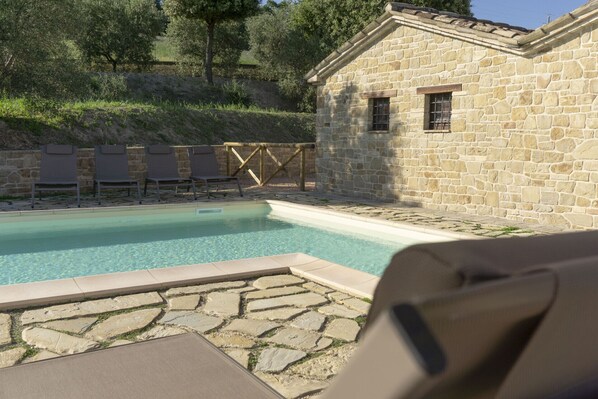 A stone building with a pool, lounge chairs, and a wooden fence.