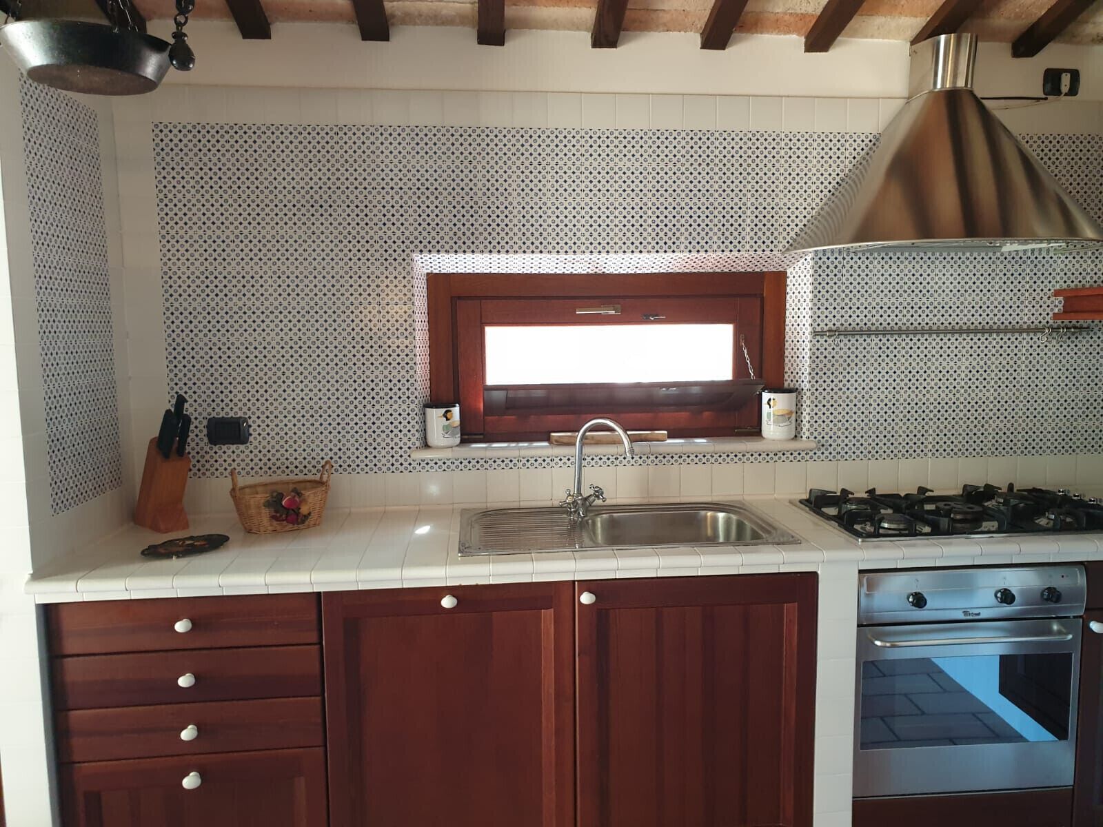 A kitchen with a stainless steel sink, a window above the sink, a gas stove, and wooden cabinets.