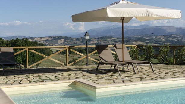 Un espace aménagé au bord de la piscine, avec vue sur les montagnes, une clôture en bois et un parasol blanc.
