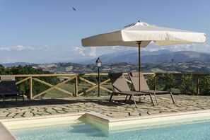A poolside area with a view of mountains, a wooden fence, and a white umbrella. - Villa alla Torre - Homelike Villas (San Severino Marche)