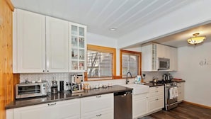 A modern kitchen with white cabinetry, a stainless steel dishwasher, a microwave, and a stove. - Red Robin W  Hot Tub Retreat Near Big Bear Lake (Big Bear Lake)