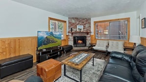 A cozy living room with a fireplace, wooden walls, a large TV, and comfortable seating. - Red Robin W  Hot Tub Retreat Near Big Bear Lake (Big Bear Lake)