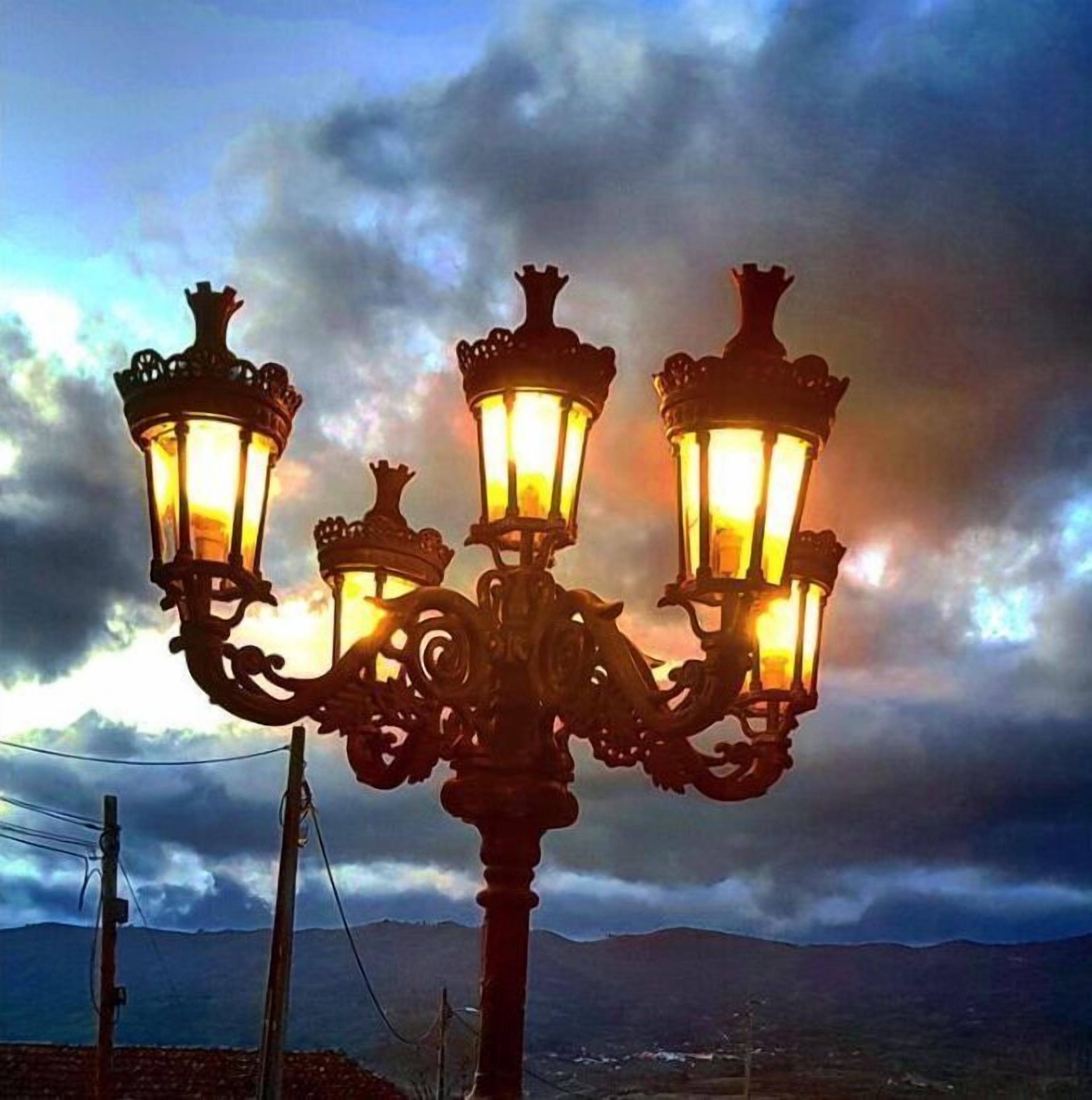 Eine Straßenlaterne mit drei Leuchten vor einem bewölkten Himmel.