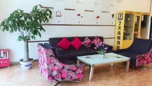 Un área de recepción con un sofá negro, sillones estampados rosas, una mesa de centro, una planta en maceta y un aparador amarillo con un letrero.