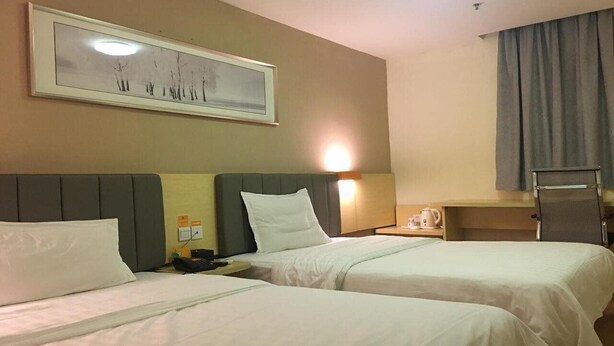 Habitación de hotel con dos camas, un cuadro en la pared, un escritorio con lámpara y una ventana con cortinas.