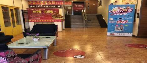 A hotel lobby with a reception desk, a staircase, and promotional posters.